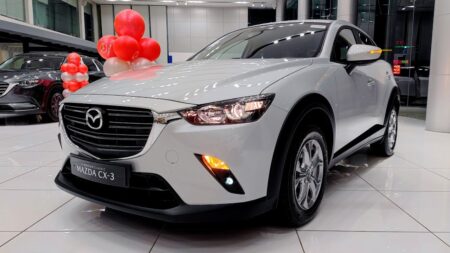 A white Mazda CX-3 on display in a showroom, adorned with red and white balloons, highlighting its modern and sleek design.