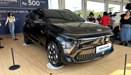 Black Hyundai Kona Electric displayed at an auto exhibition with people in the background.