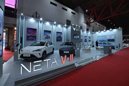 Booth showcasing Neta V-II electric cars at the Jakarta Auto Fair 2024, with two cars displayed on a platform, posters on the walls, and the Neta logo above.