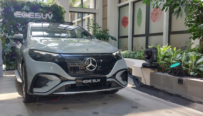 Mercedes-Benz EQE SUV displayed indoors surrounded by plants, with a sign indicating the model name, at an Autoini event in Indonesia.