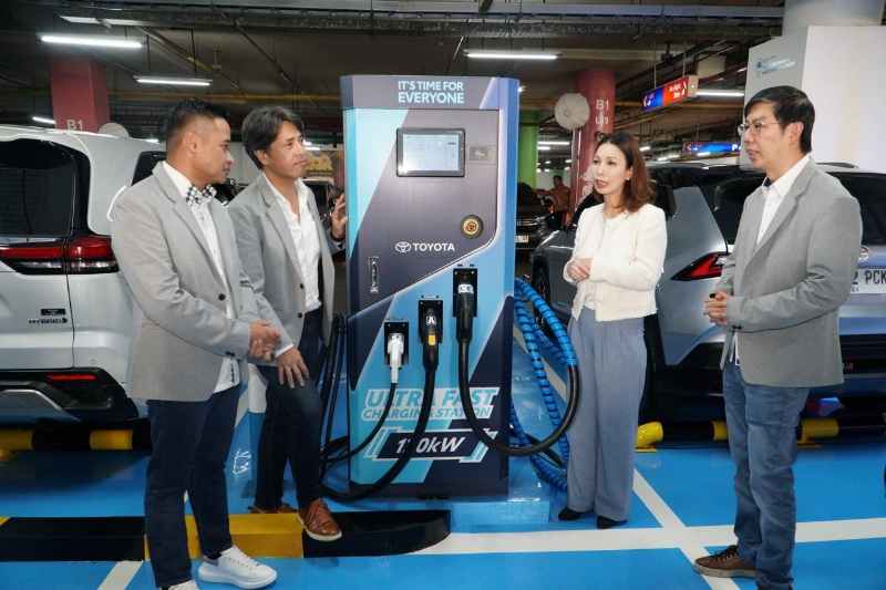 A group of people standing around a Toyota-branded EV charging station in a parking area.