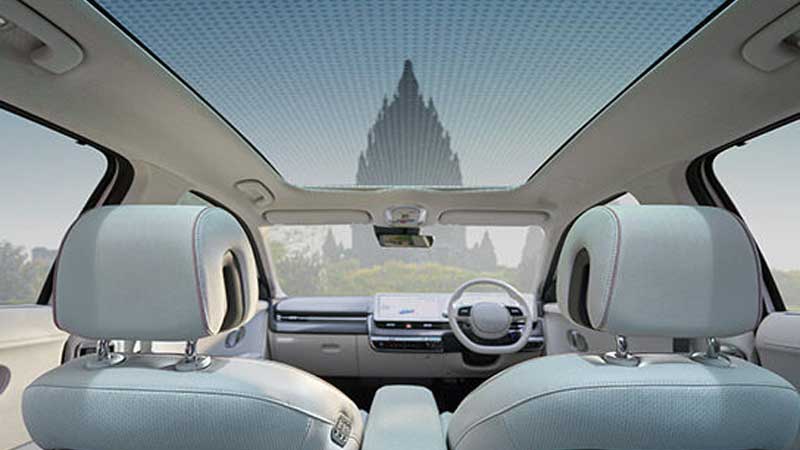 Hyundai Ioniq 5 interior with panoramic sunroof showcasing a clear sky with a building in the distance.