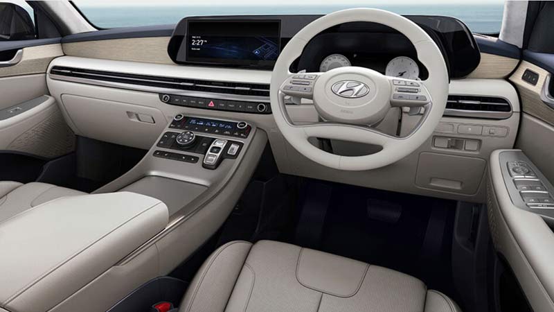Interior of a Hyundai Palisade SUV with a beige and black color scheme, featuring a large central touchscreen, a leather-wrapped steering wheel, and comfortable-looking seats.